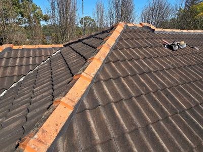 Fresh sand-and-cement bedding being laid under ridgecaps on a tile roof